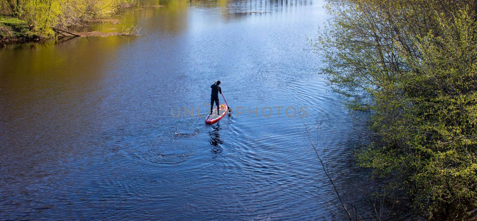 A man is floating on a paddle Board on the spring river. I can't see his face.
