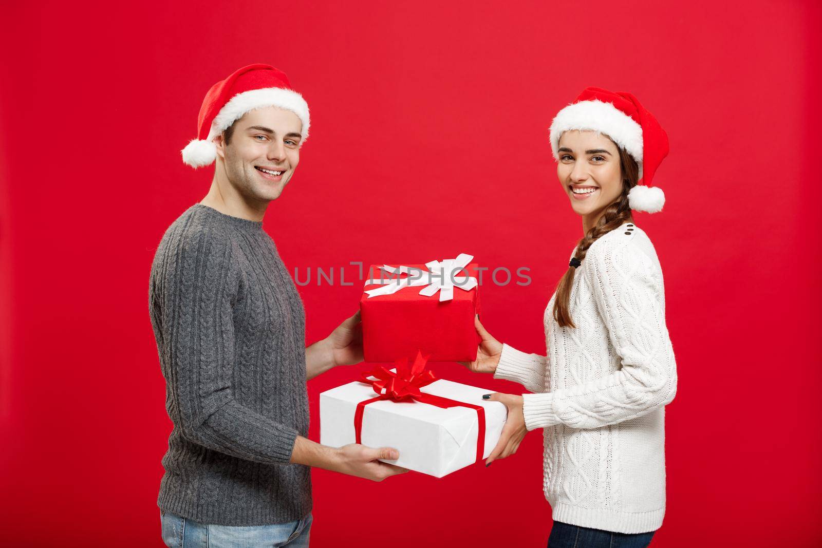 Christmas Concept - Young attractive couple giving gifts to each other celebrating in Christmas day.