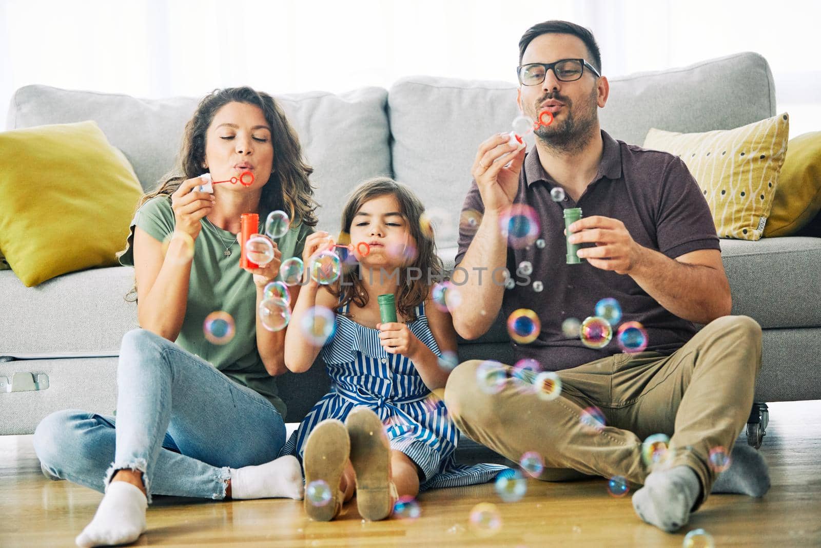 Family having fun blowing soap bubbles on sofa at home
