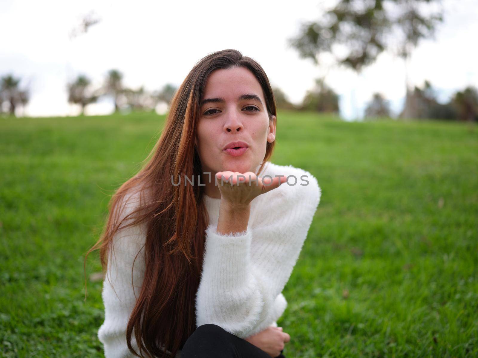 Front view of a young girl in love in the park blows a kiss to the camera. Concept of emotions.