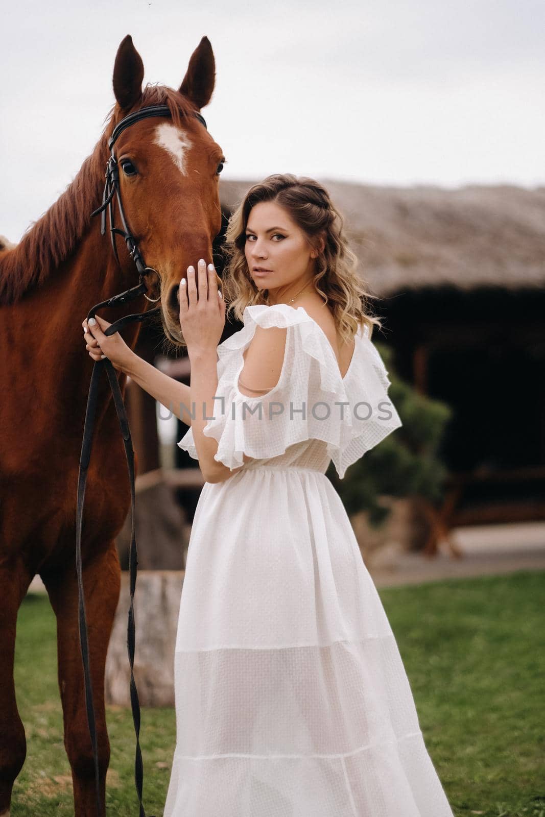 Beautiful girl in a white sundress next to a horse on an old ranch.