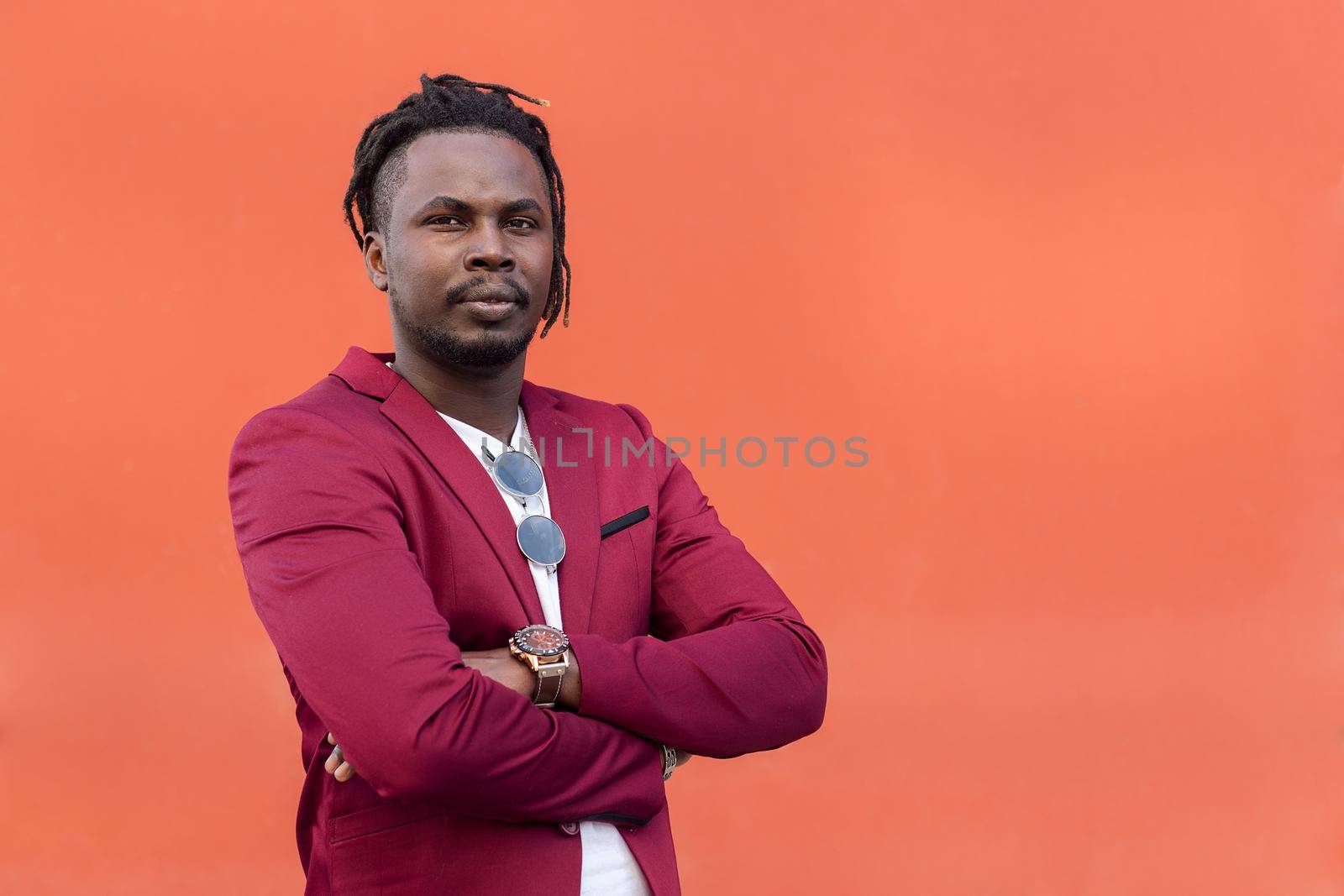 stylish black businessman in suit posing looking at camera with arms crossed in front of red background, copy space for text