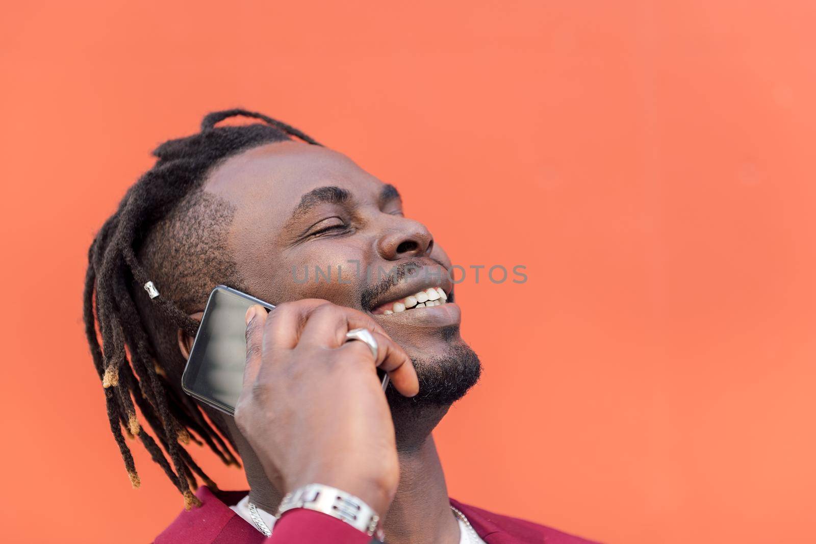 portrait of a stylish black businessman laughing and talking on phone in front of red background, copy space for text, concept of technology and communication