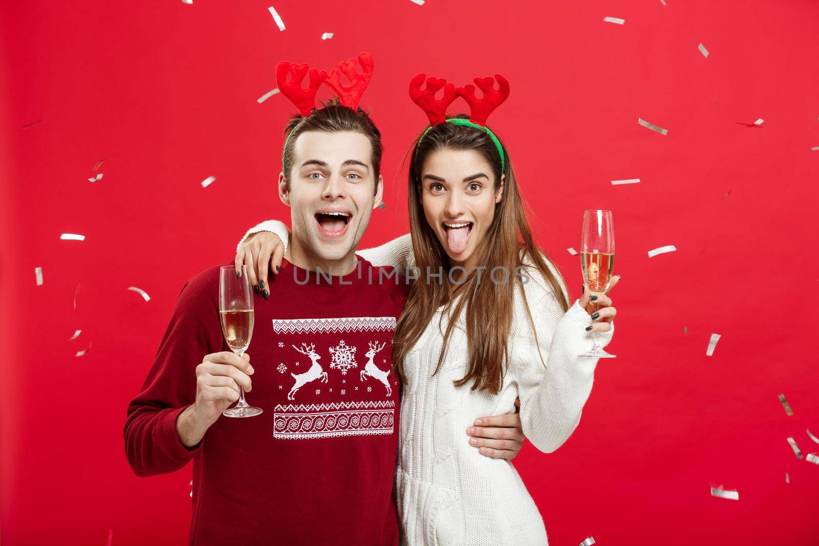 Christmas Concept - Happy caucasian man and woman in reindeer hats celebrating christmas toasting with champagne flutes, congratulating on xmas by Benzoix