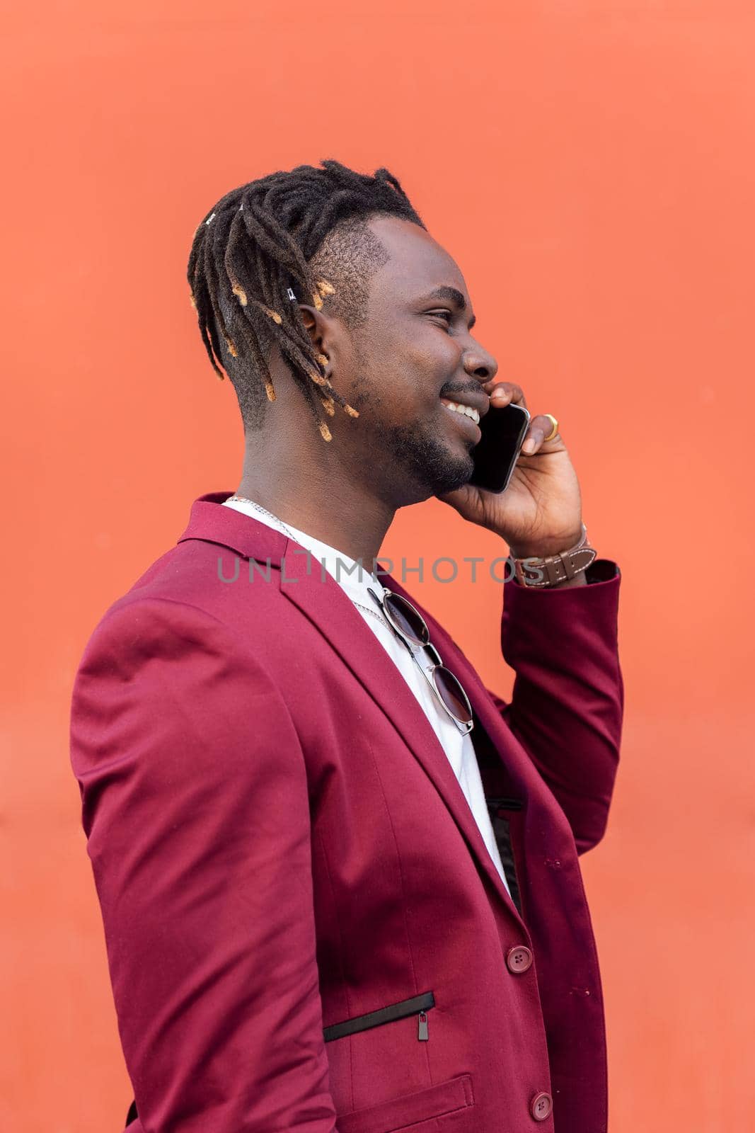vertical profile portrait of a stylish black businessman in suit smiling and talking on phone in front of red background, copy space for text, concept of technology and communication