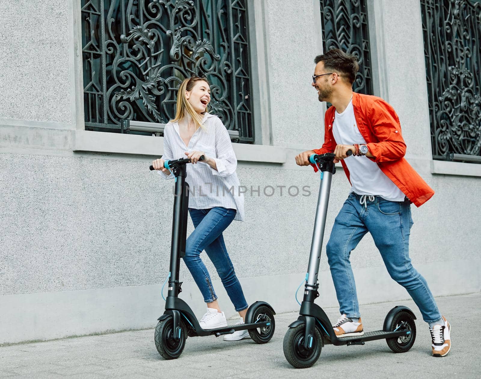 Young couple having fun driving electric scooter through the city