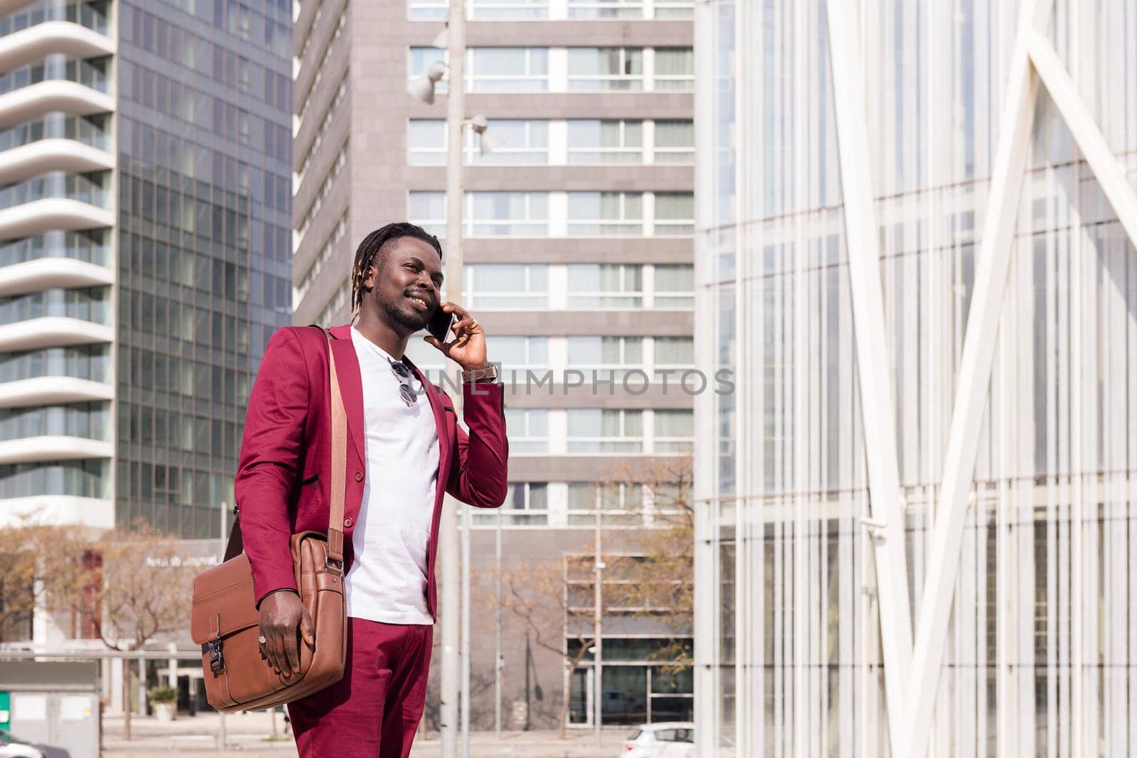 elegant black businessman with briefcase walks through the city financial downtown talking on phone, concept of technology and communication, copy space for text