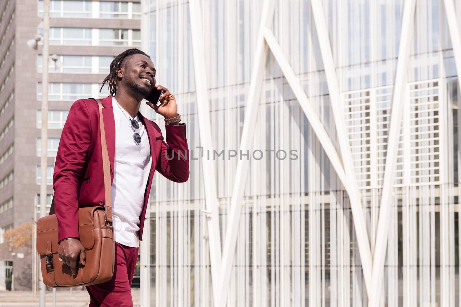 smiling black businessman with briefcase walks through the city financial downtown talking on phone, concept of technology and communication, copy space for text