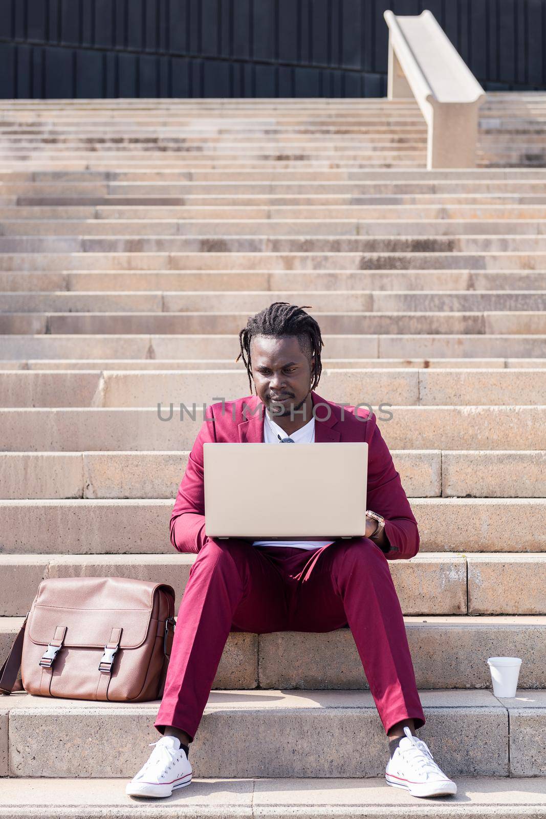 elegant african businessman works with his laptop sitting on a staircase in the city, technology and remote work concept, copy space for text