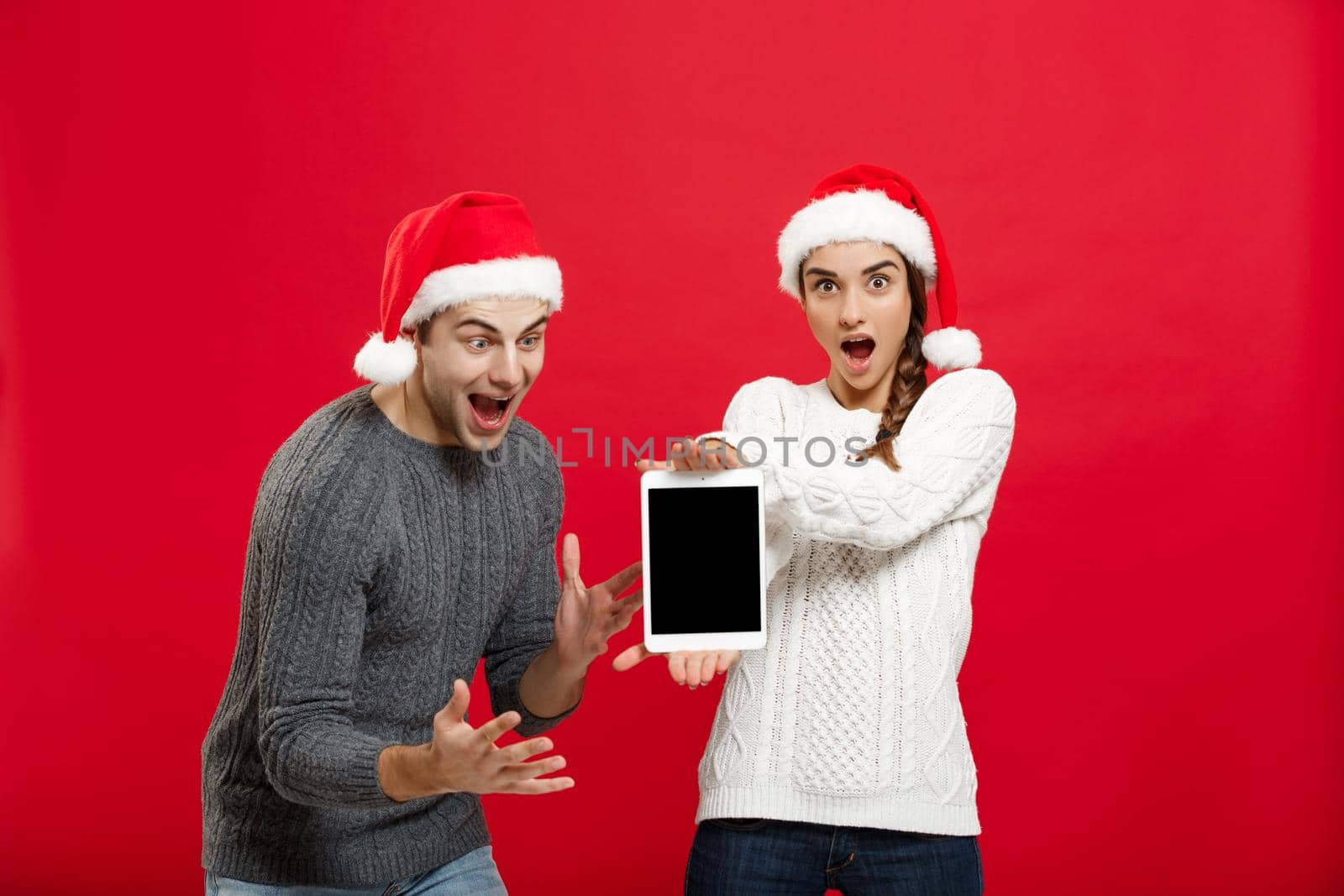 Christmas concept - Happy young couple in christmas sweaters surprising something in digital tablet by Benzoix