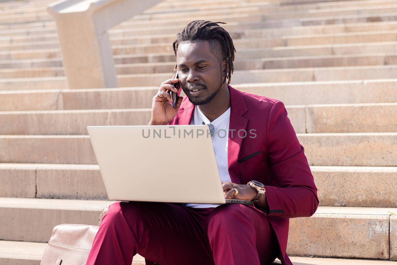 african man working with computer laptop and phone sitting on city stairs, concept of technology and remote work