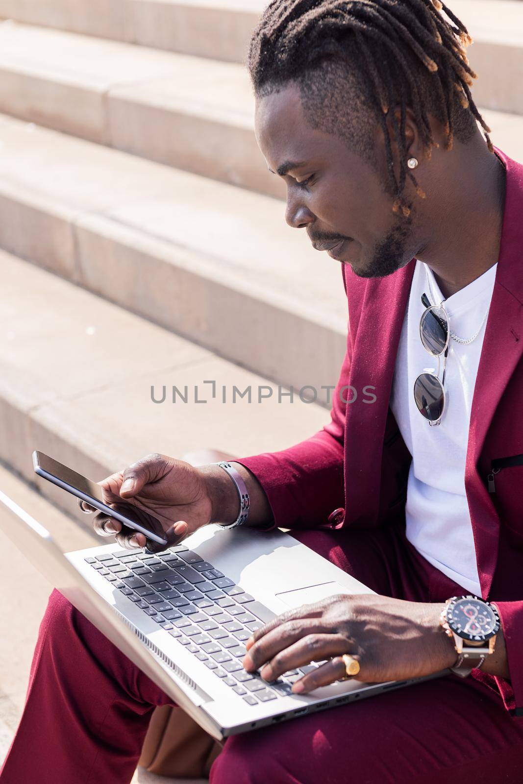 vertical photo of a black businessman using a smart phone and computer laptop, technology and remote work concept, copy space for text