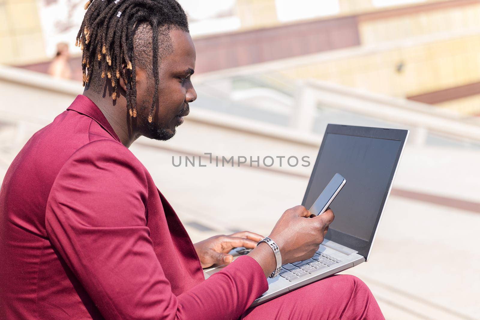 elegant black businessman works outdoors with laptop and phone, technology and remote work concept