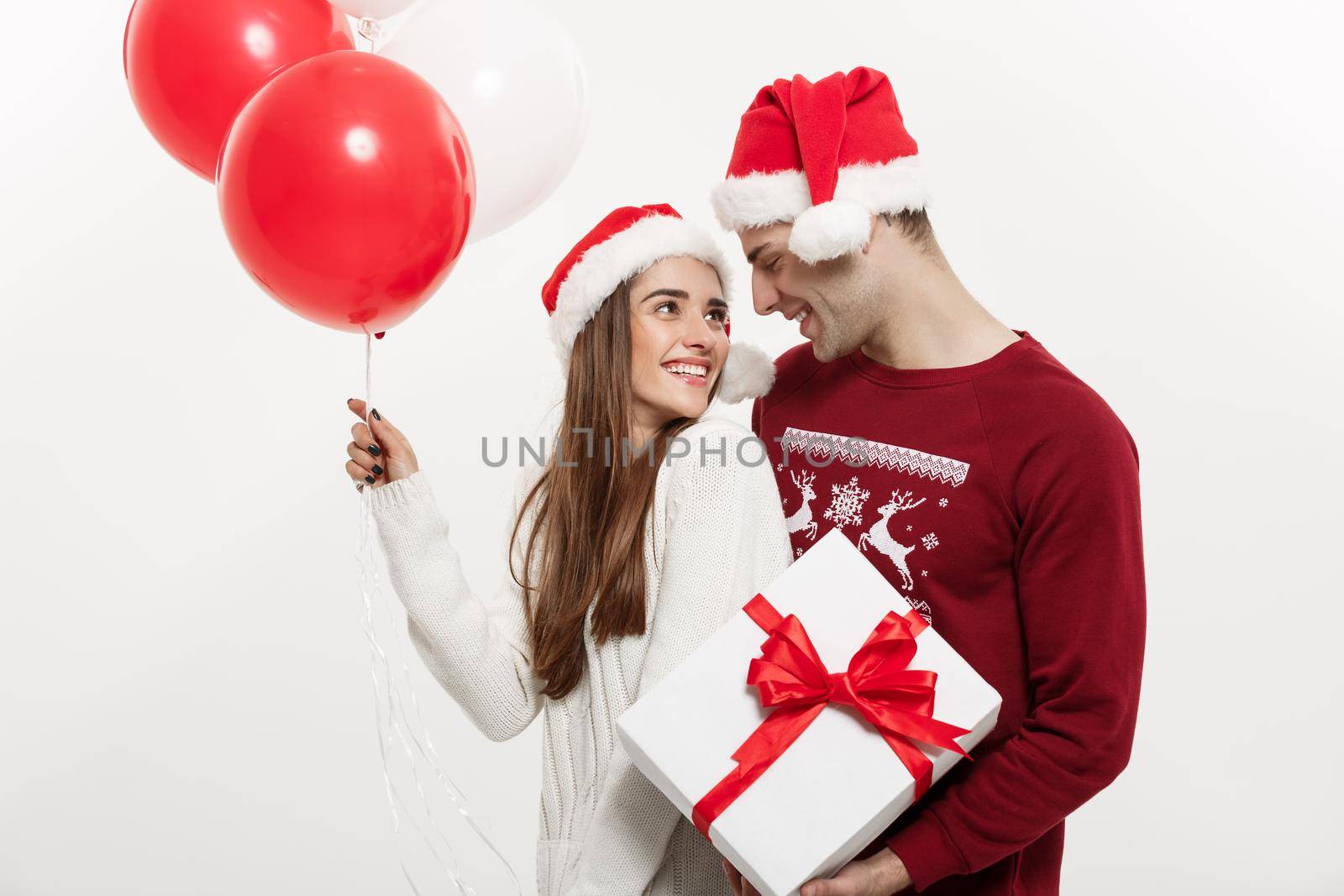 Christmas Concept - Young girlfriend holding balloon is hugging and playing with her boyfriend doing a surprise on Christmas.