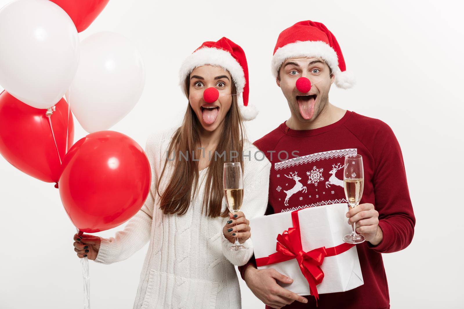 Christmas Concept - Young caucasian couple holding gifts,champagne and balloon making funny face on Christmas by Benzoix