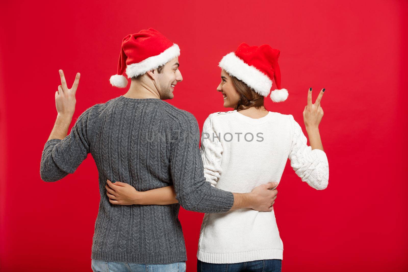 Christmas Concept - back view of portrait lovely young couple showing two finger gesture by Benzoix