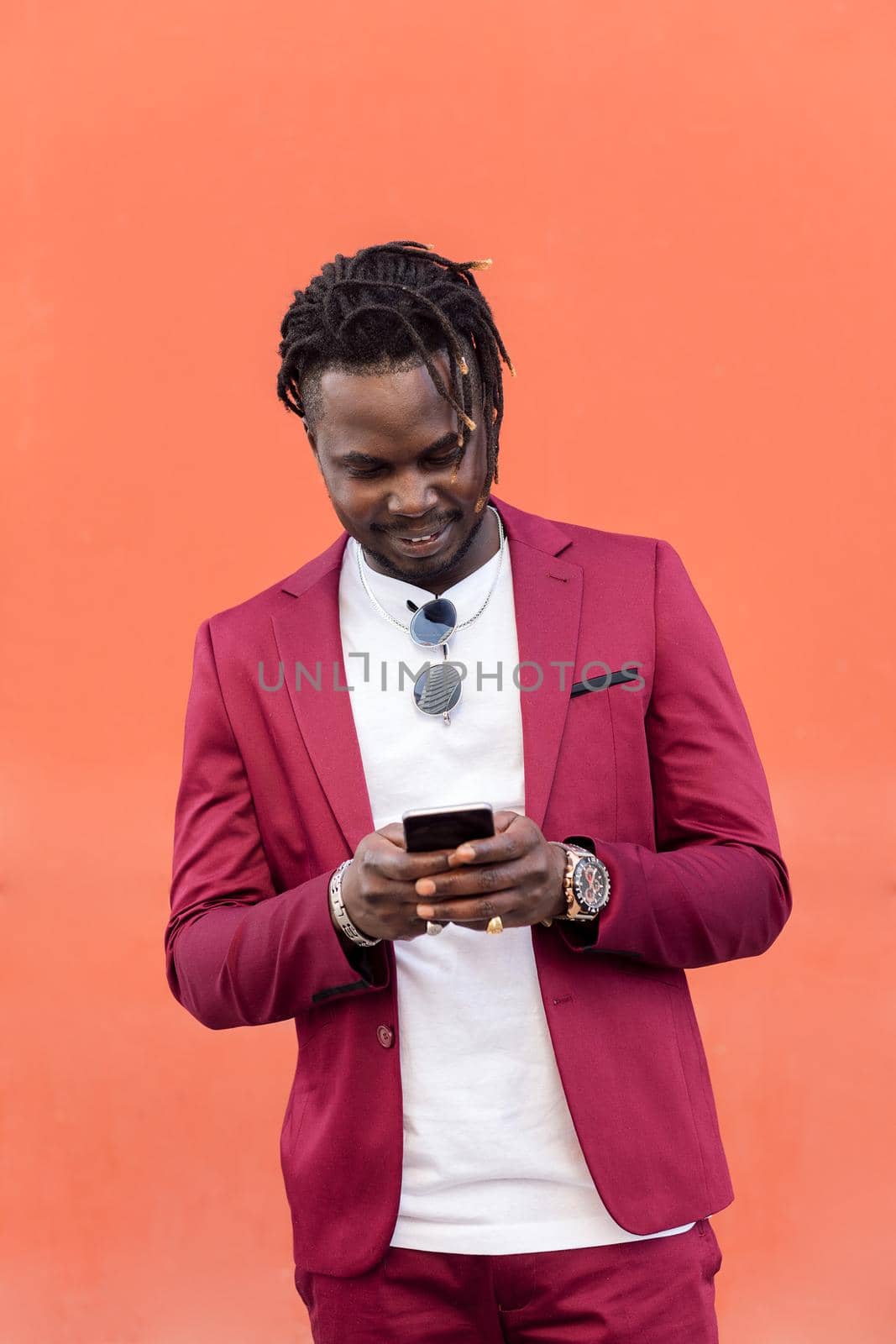 vertical photo of a stylish african businessman in suit typing a message on his smart phone in front of a red background, copy space for text, concept of technology and communication