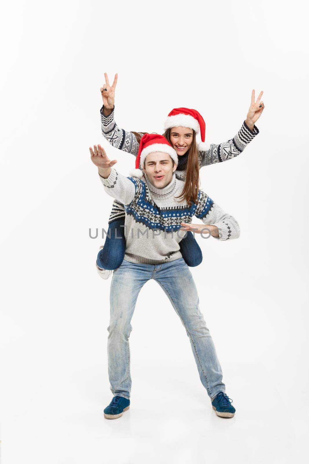 Christmas Concept - Young happy couple in sweaters enjoying piggyback ride isolated on white grey background.