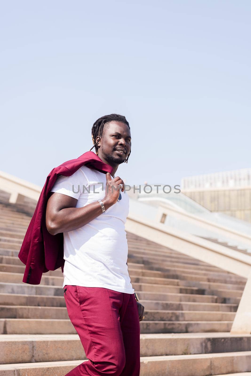 vertical photo of a stylish black man walking down a city staircase with his jacket over his shoulder, urban lifestyle concept, copy space for text