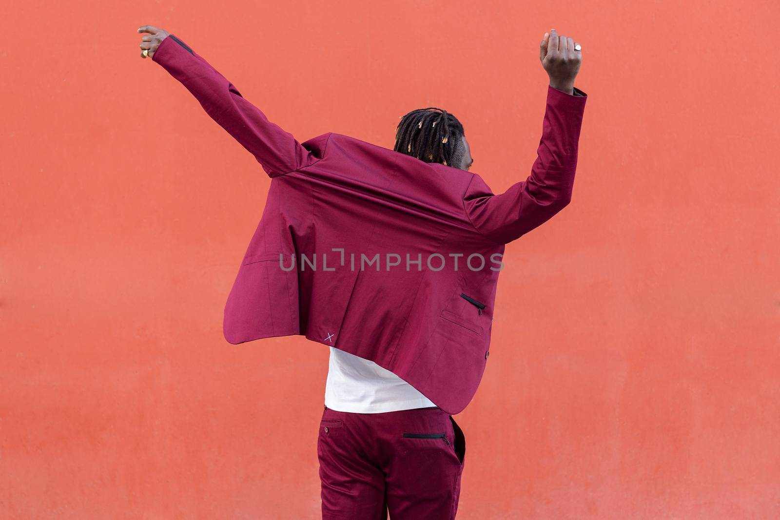 rear view of a black man putting on a blazer on a red background, concept of elegance and fashionable lifestyle