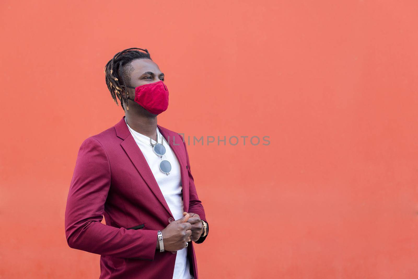 elegant african man with protective mask to match his suit on a red background, copy space for text, concept of elegance and fashionable lifestyle