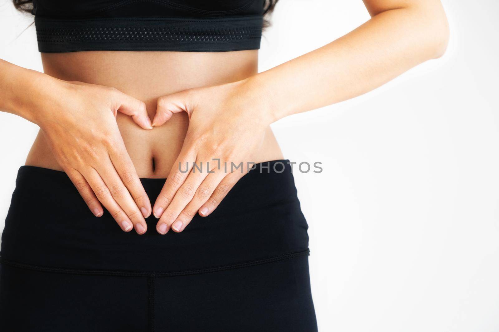Close up shot of young woman in sportswear making heart shape gesture at her abdomen. Dieting weight loss and healthy nutrition concept.