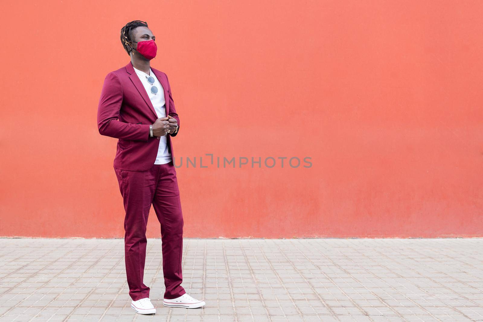 handsome black man with protective mask to match his suit on a red background, concept of elegance and fashionable lifestyle