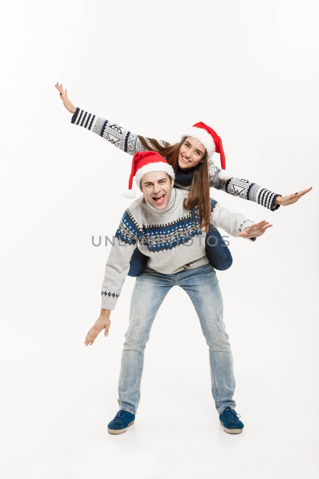 Christmas Concept - Full-length Young happy couple in sweaters enjoying piggyback ride isolated on white grey background by Benzoix