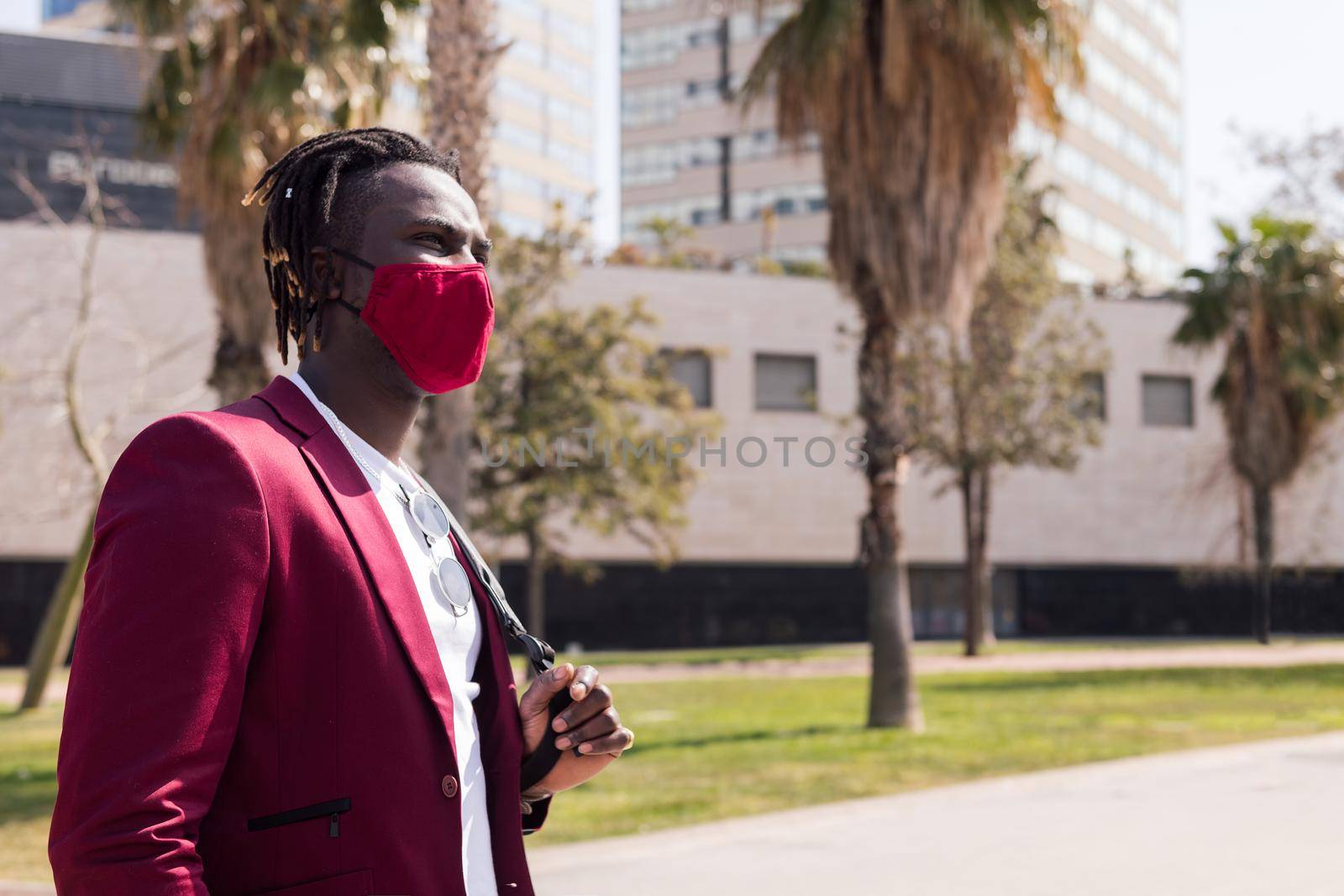 african businessman walking around the city with a red mask to match his suit, concept of elegance and fashionable lifestyle, copy space for text
