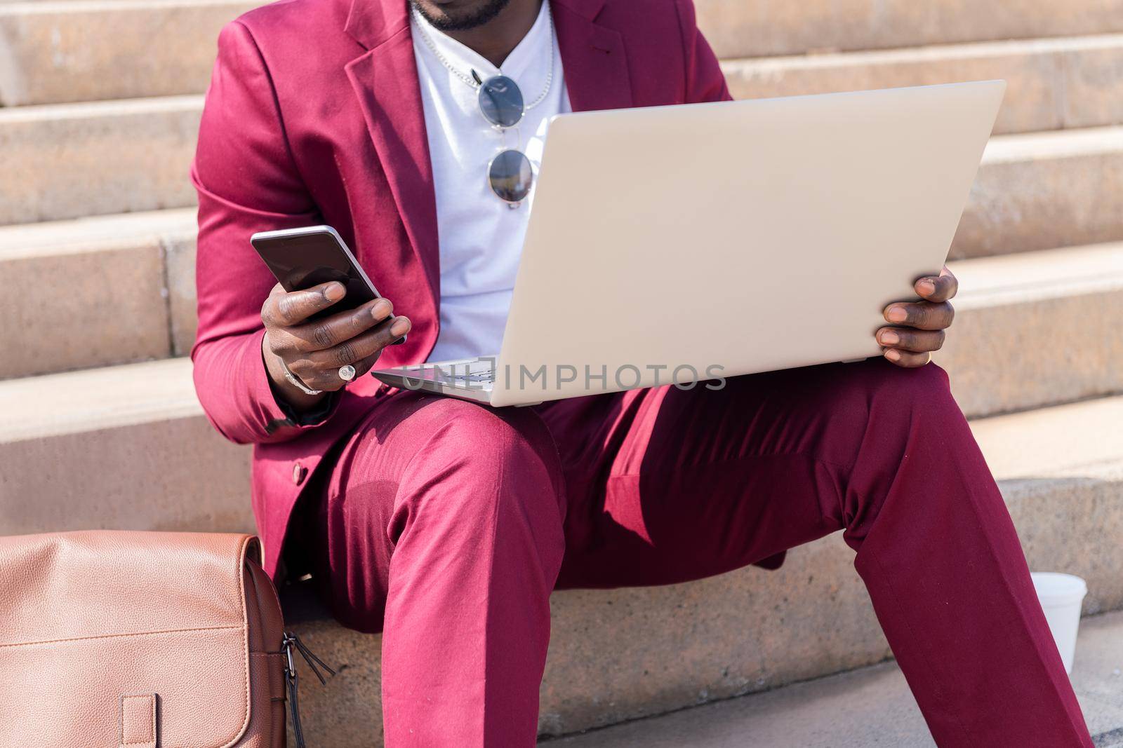 unrecognizable elegant black businessman working outdoors with laptop and smart phone, technology and remote work concept