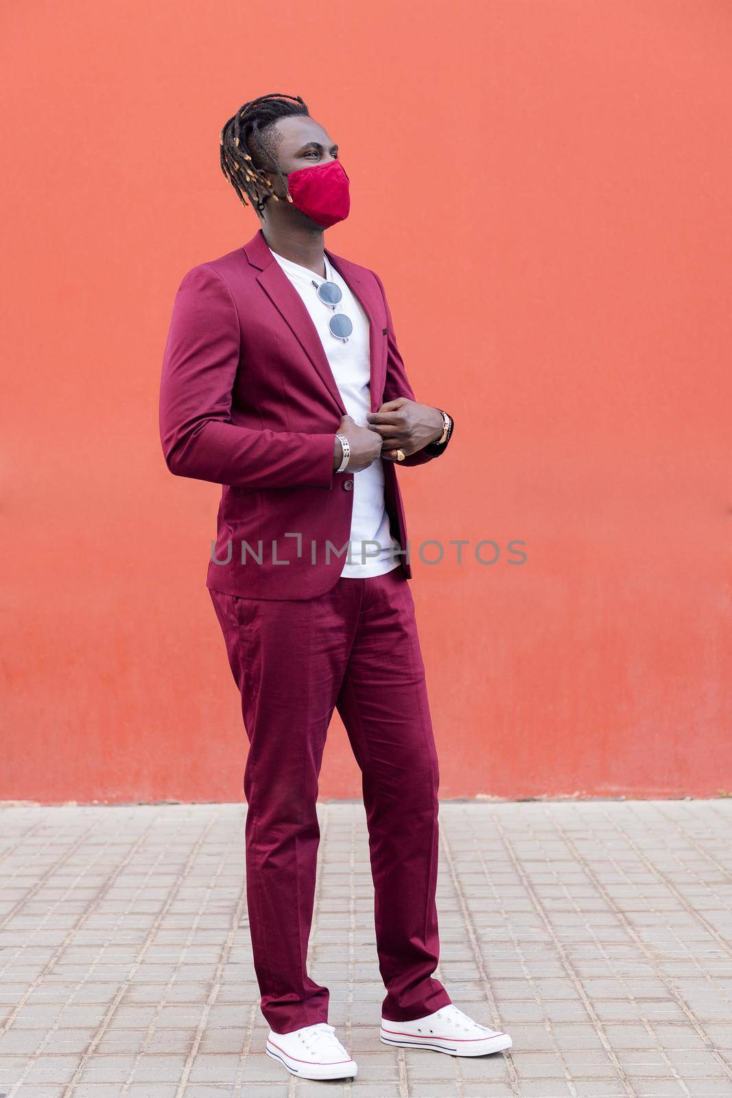 vertical photo of a handsome black man with protective mask to match his suit on a red background, concept of elegance and fashionable lifestyle