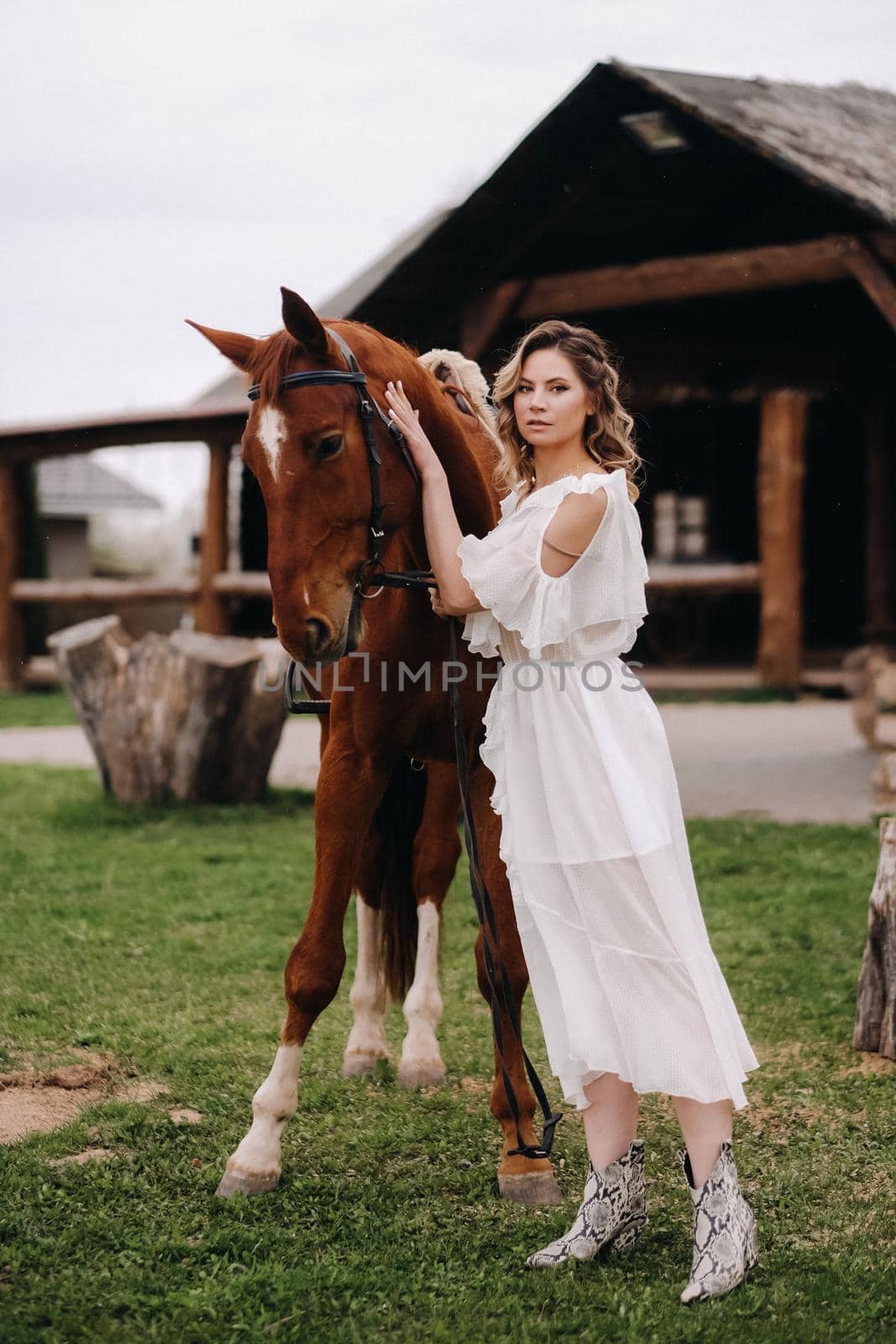 Beautiful girl in a white sundress next to a horse on an old ranch.