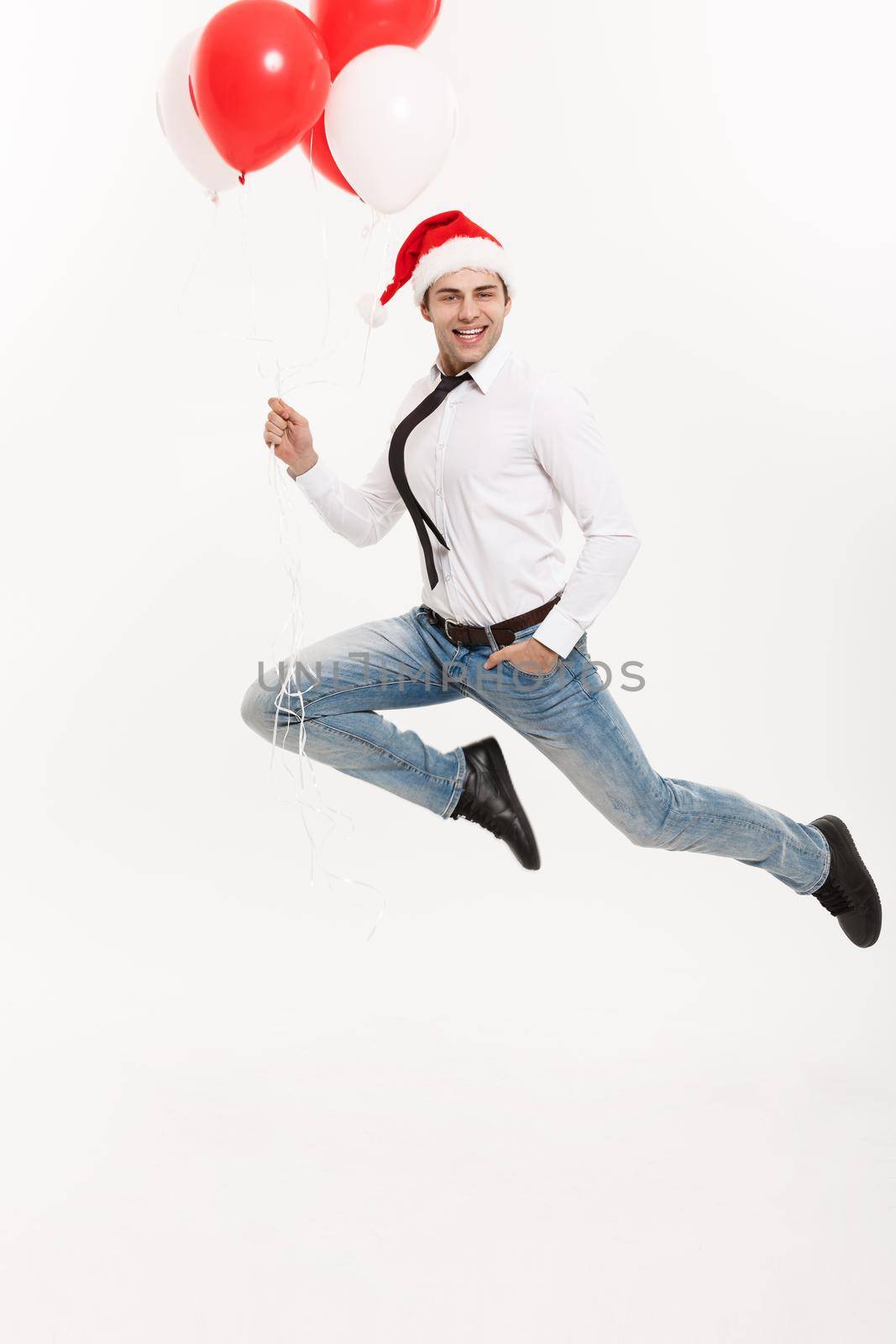 Christmas Concept - Handsome Business man jumping for celebrating merry christmas and happy new year wear santa hat with red balloon. by Benzoix