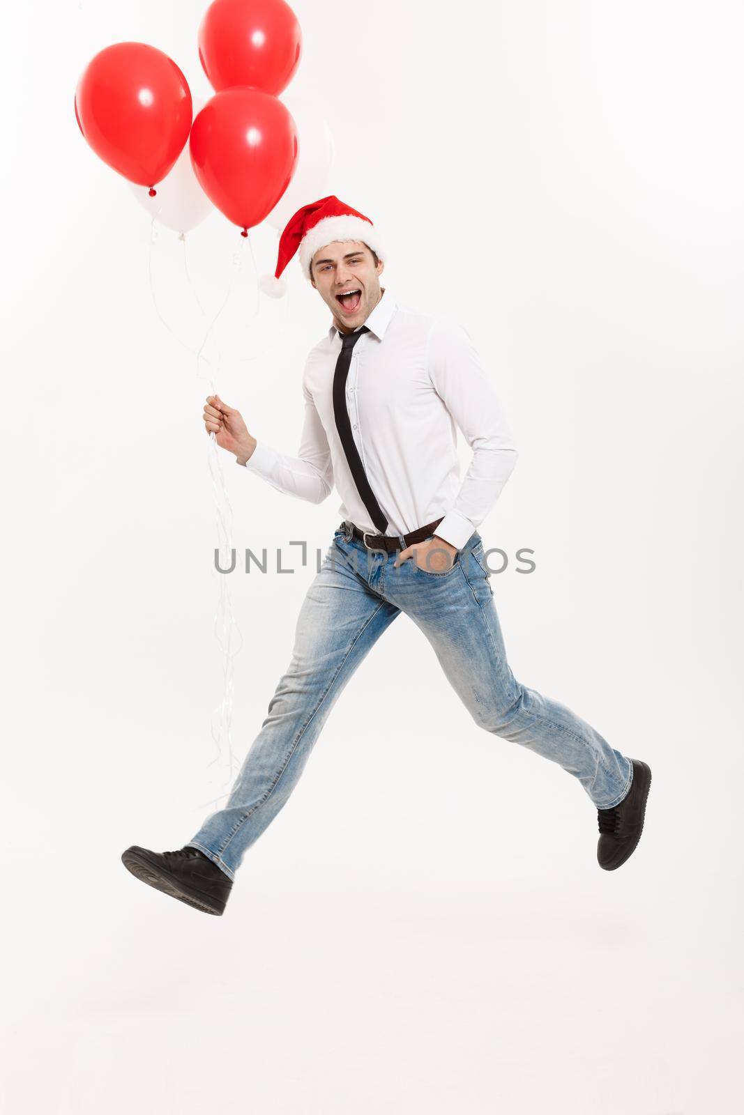 Christmas Concept - Handsome Business man jumping for celebrating merry christmas and happy new year wear santa hat with red balloon. by Benzoix