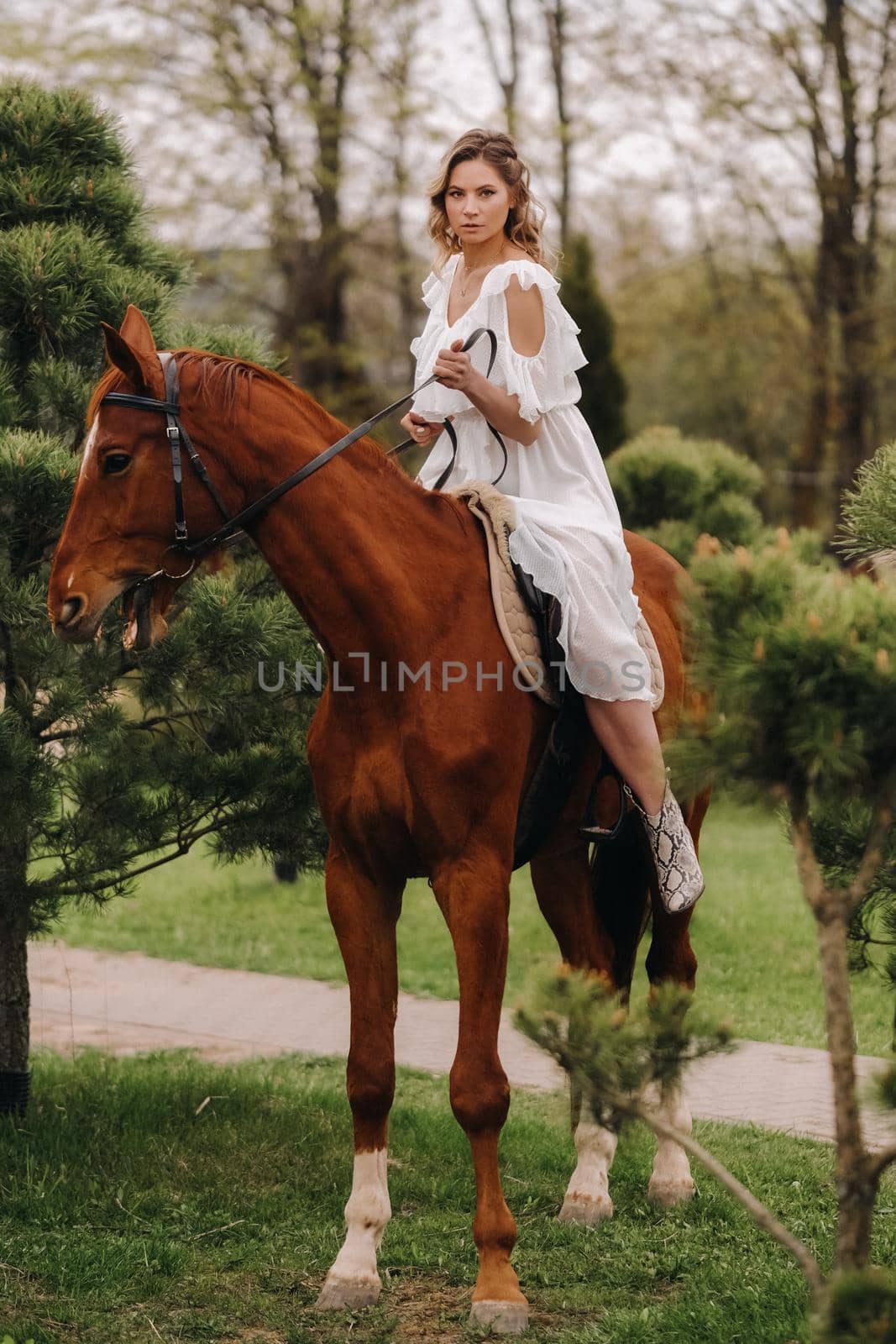 A woman in a white sundress riding a horse near a farm.