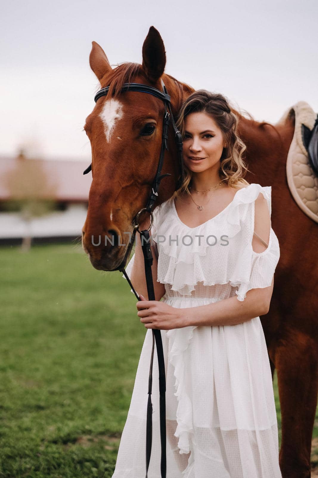 Beautiful girl in a white sundress next to a horse on an old ranch.