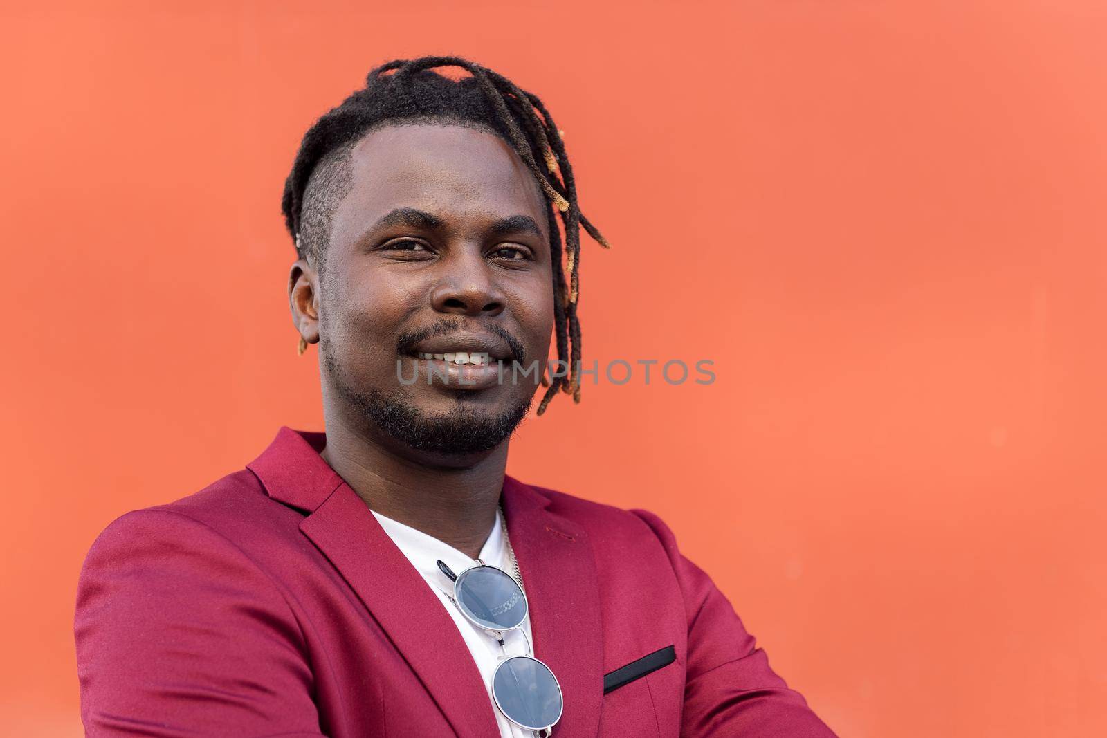 portrait of a stylish black businessman posing looking at camera with arms crossed in front of red background, copy space for text