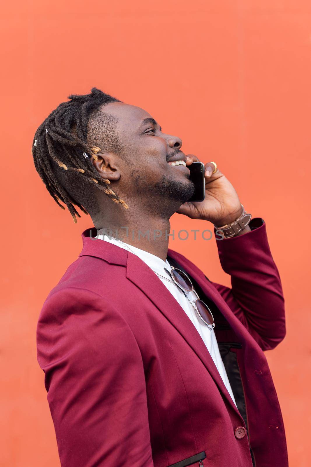 vertical profile portrait of a stylish african businessman in suit laughing and talking on phone in front of red background, copy space for text, concept of technology and communication