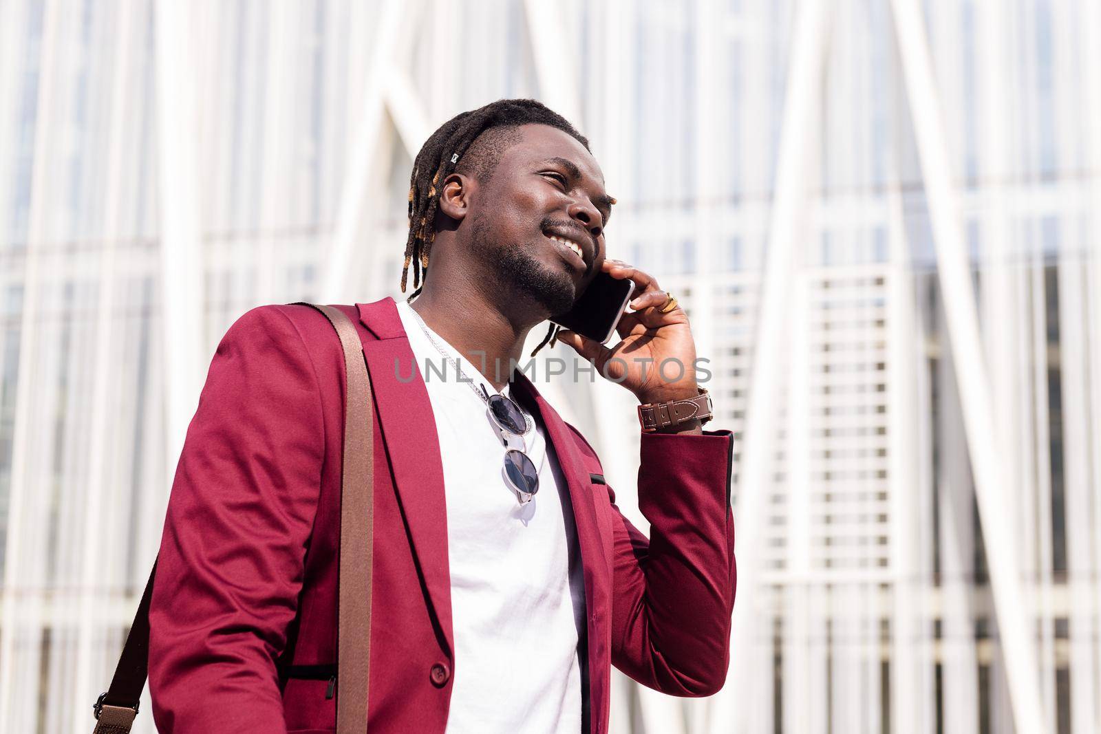 smiling african businessman talking on phone at the city financial downtown, concept of technology and communication, copy space for text