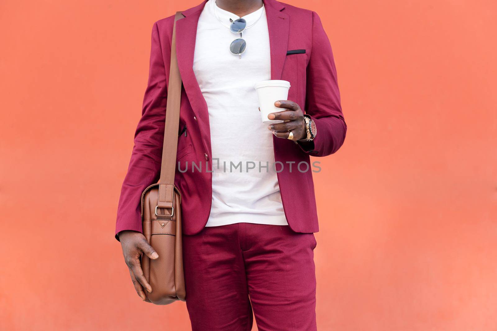 unrecognizable elegant black businessman dressed in suit with briefcase holds coffee in his hand in front of red background, copy space for text