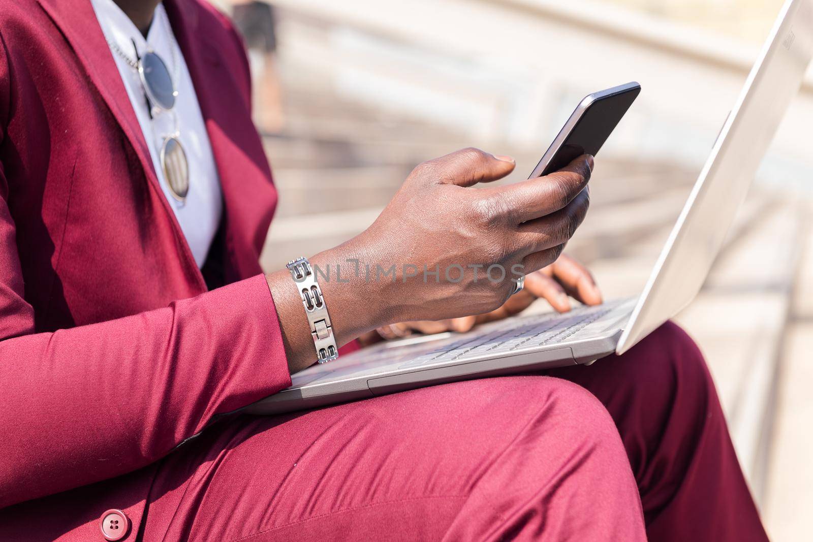 detail of the hand of an african businessman using a smart phone and computer laptop, technology and remote work concept