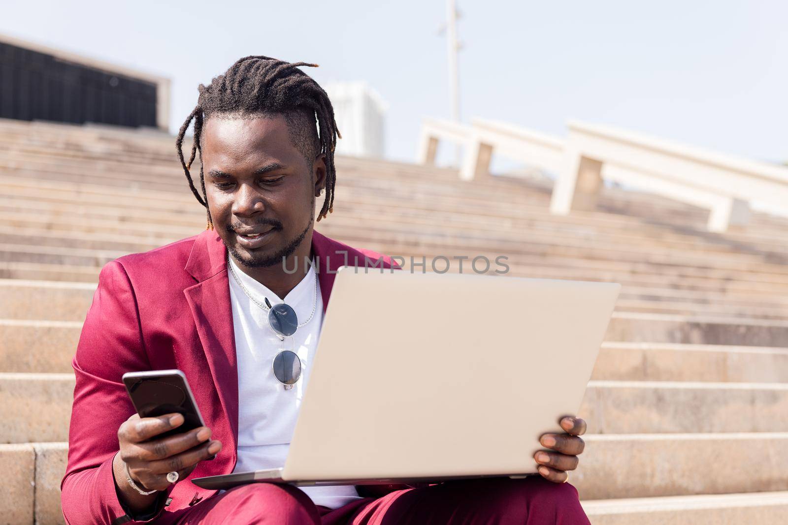 stylish african businessman working outdoors with laptop and smart phone, technology and remote work concept, copy space for text