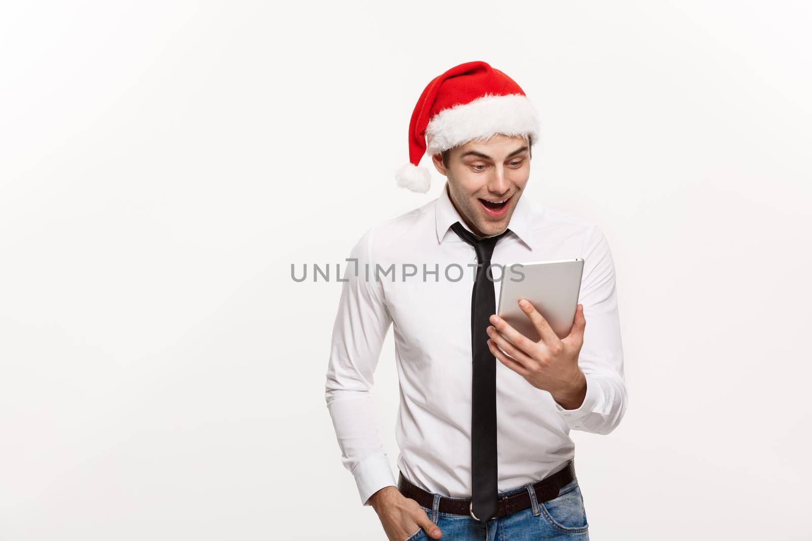 Christmas Concept - Handsome Business man wear santa hat playing tablet with surprising facial expression.