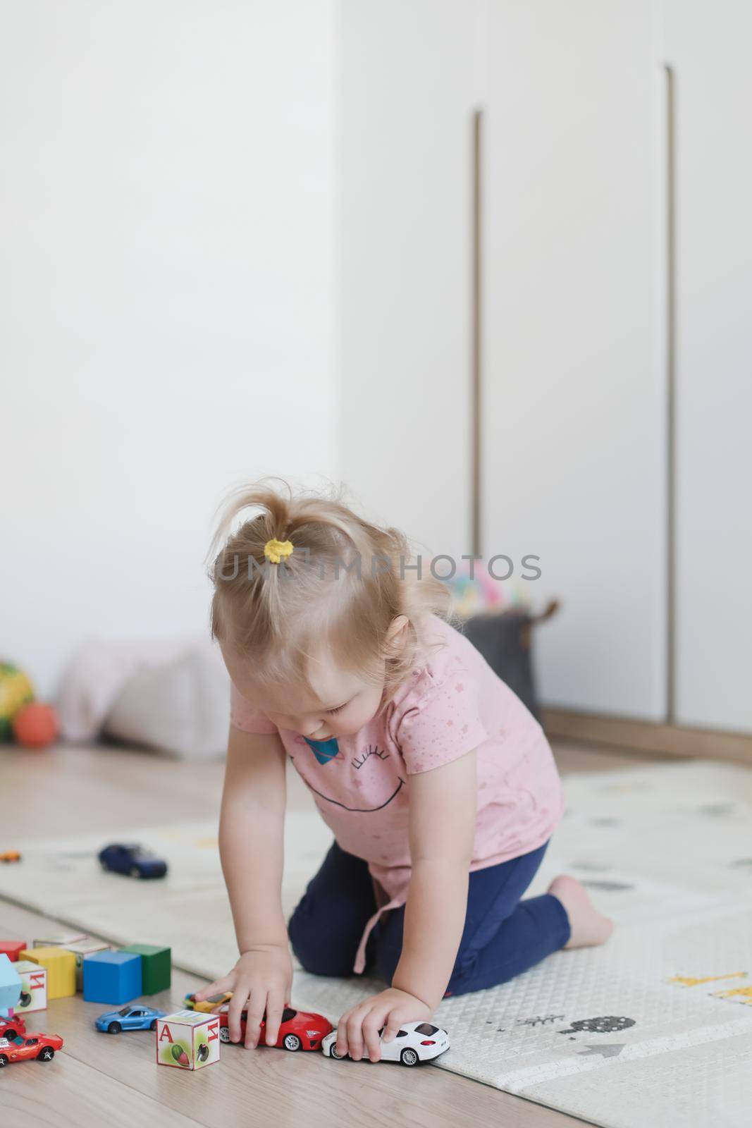 a little funny girl plays with cubes and toys on the floor in the nursery by paralisart