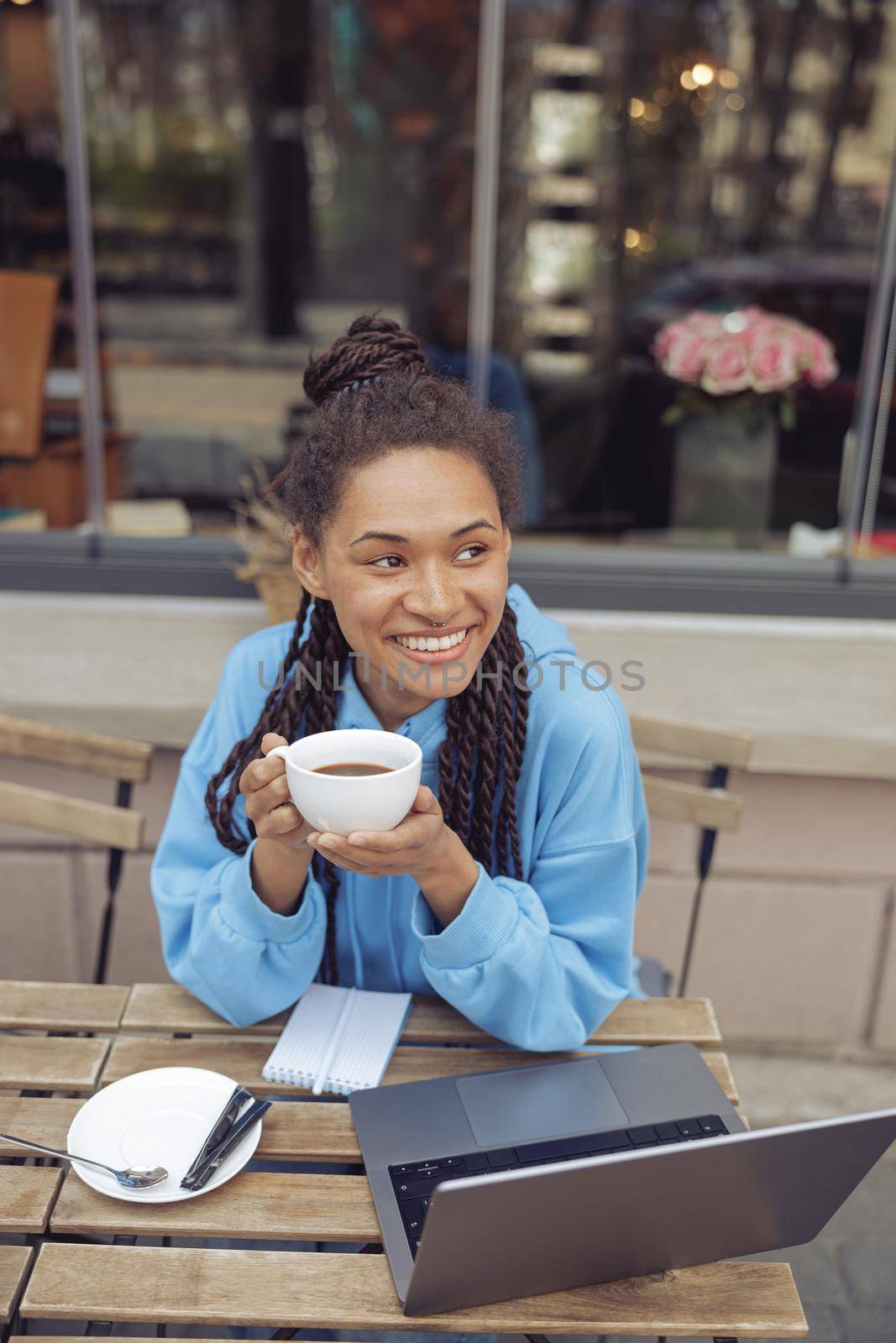 Beautiful young mixed-race stylish woman with piercing holding coffee, smiling. Top view. Vertical.