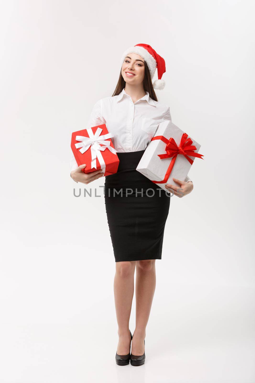 Business Concept - Beautiful young caucasian business woman with santa hat holding gift boxes with copy space on side.