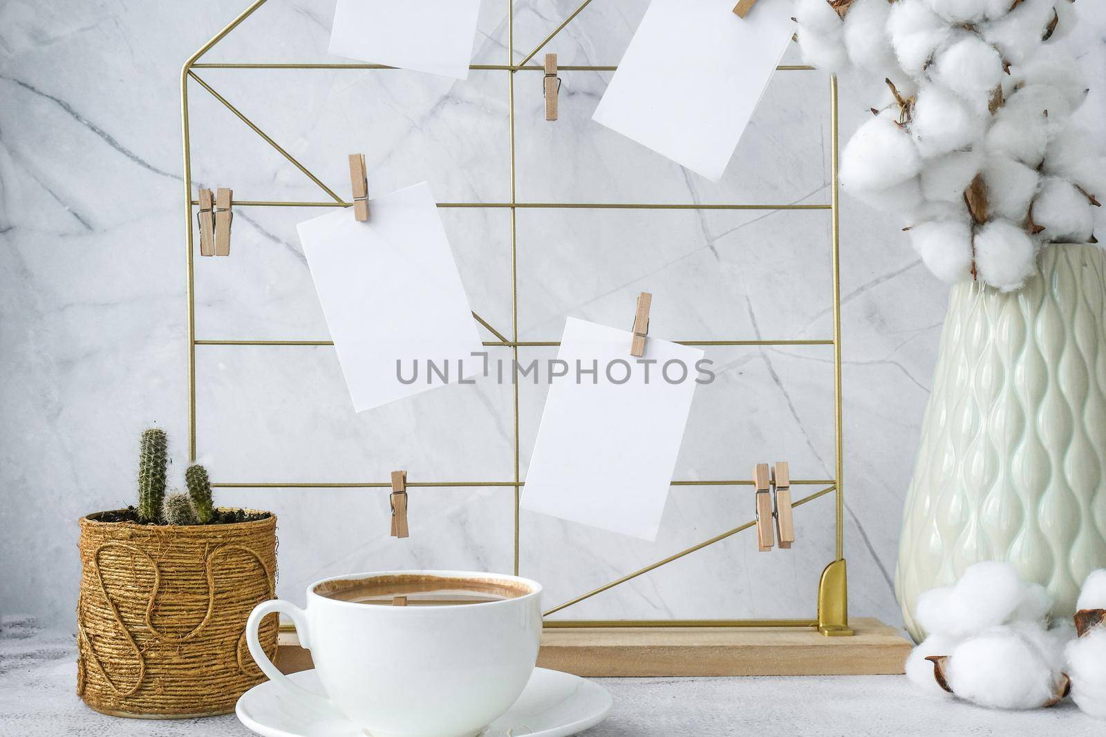 White home office room interior, bloggers workplace. Cup of coffee. Mood board with postcards and reminders mockup. Cotton branches in a vase, interior decoration. Freelance workplace by anna_stasiia