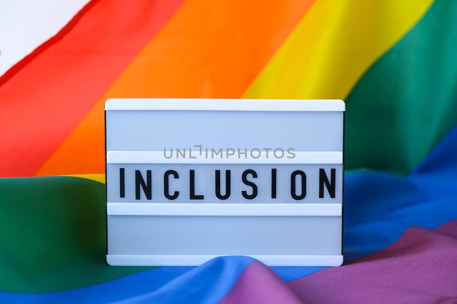 Rainbow flag with lightbox and text INCLUSION. Rainbow lgbtq flag made from silk material. Symbol of LGBTQ pride month. Equal rights. Peace and freedom. Support LGBTQ community