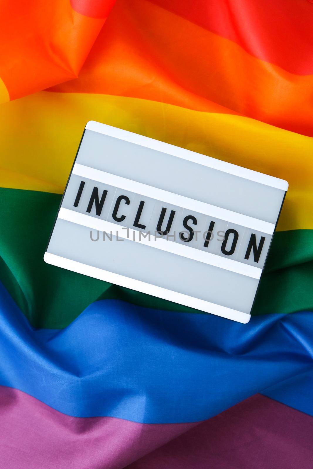 Rainbow flag with lightbox and text INCLUSION. Rainbow lgbtq flag made from silk material. Symbol of LGBTQ pride month. Equal rights. Peace and freedom. Support LGBTQ community