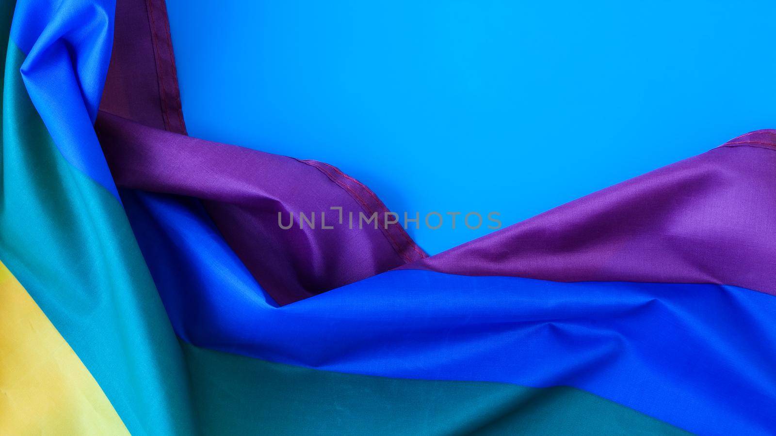 Rainbow flag on blue background with copy space. Rainbow lgbtq flag made from silk material. Symbol of LGBTQ pride month. Equal rights. Peace and freedom by anna_stasiia